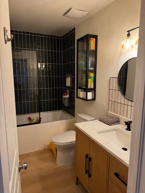 Completed bathroom with black tile, new vanity and wood-look flooring